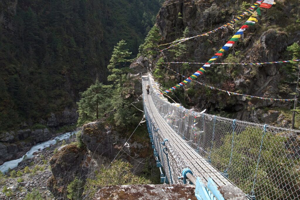 Puente colgante metálico sobre un río de aguas grises encajado entre laderas boscosas