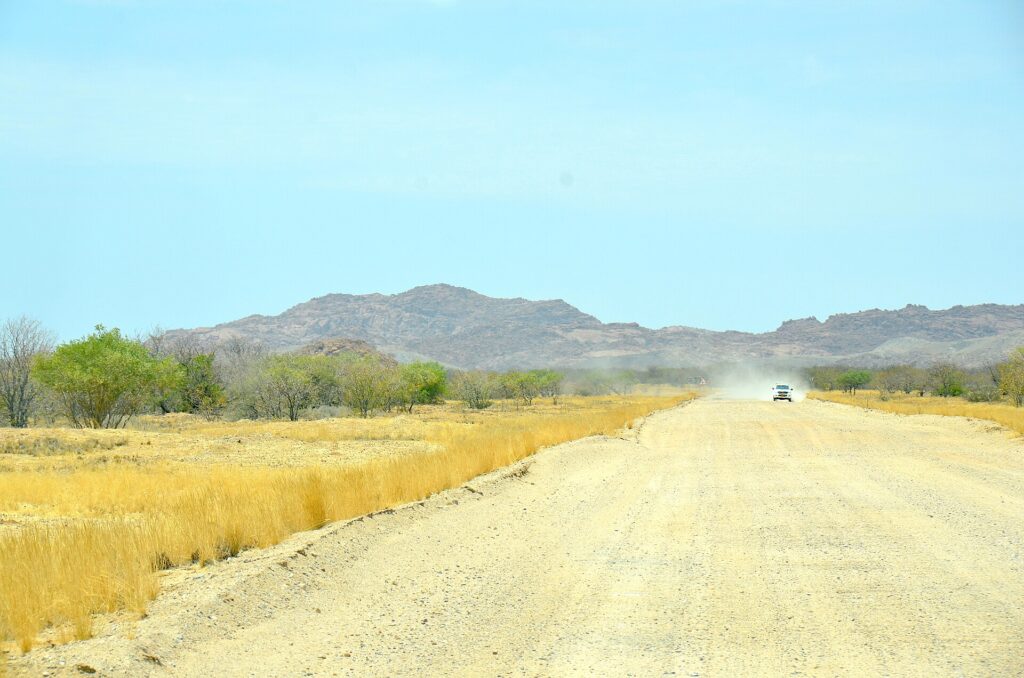 Pista de grava recta que cruza una llanura seca con montañas bajas al fondo