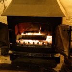 Estufa de leña encendida en el salón de una cabaña de madera con nieve fuera