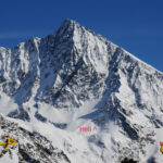 Helicóptero de rescate suspendido sobre una ladera rocosa con nieve en las cotas altas