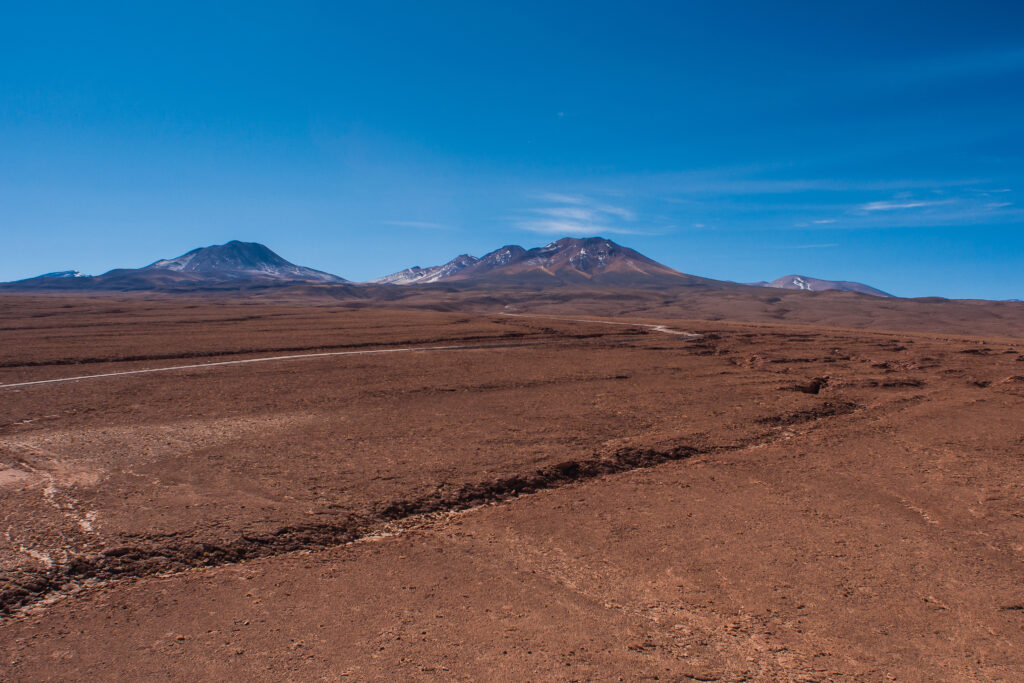 Rodadas de vehículo marcadas sobre suelo pedregoso con montañas bajas en el horizonte