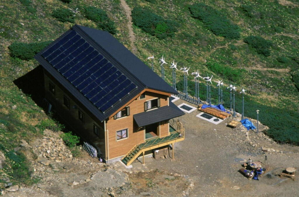 Cabaña de montaña roja con tejado de hierba junto a un lago en terreno abierto