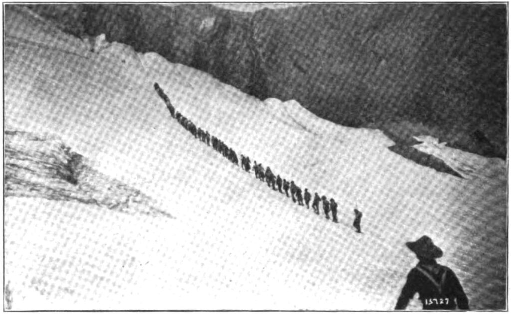 Caminantes en fila cruzando una zona de nieve dura junto a bloques de hielo