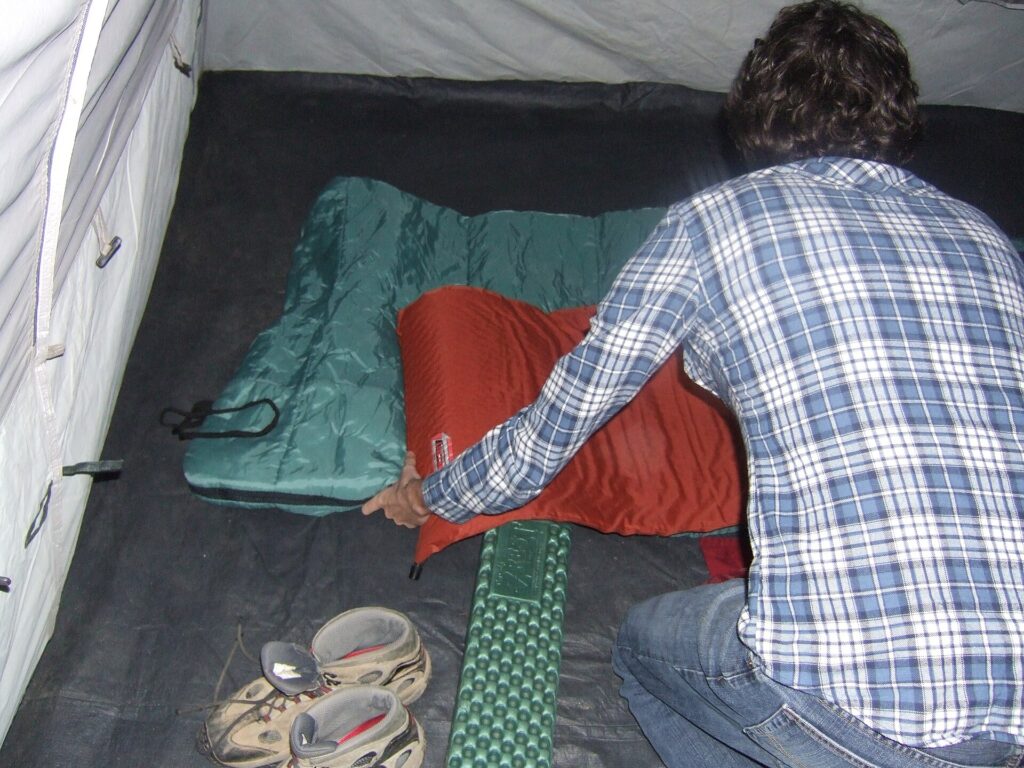 Saco de dormir extendido sobre una esterilla hinchable junto a una esterilla de espuma