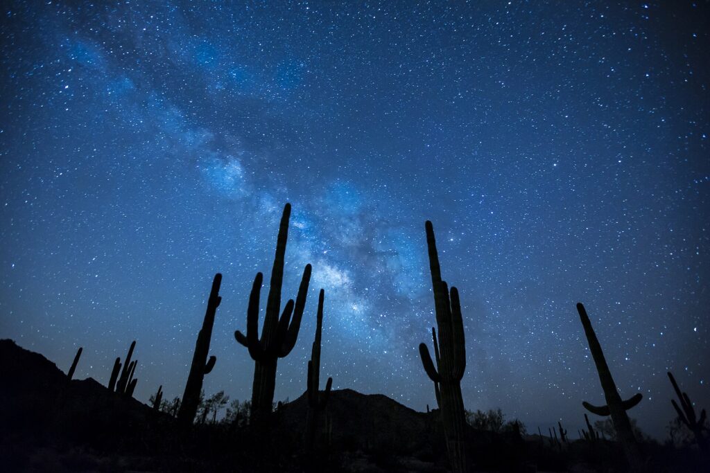 Cielo estrellado sobre una cresta de duna con una tienda iluminada en primer término