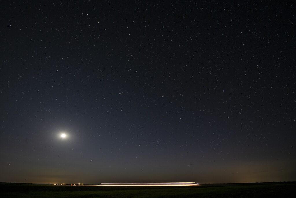 Cielo nocturno con miles de estrellas sobre una silueta de dunas y una tienda iluminada
