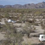 Campamento pequeño entre dunas con la primera luz rasante y sombras largas sobre la arena