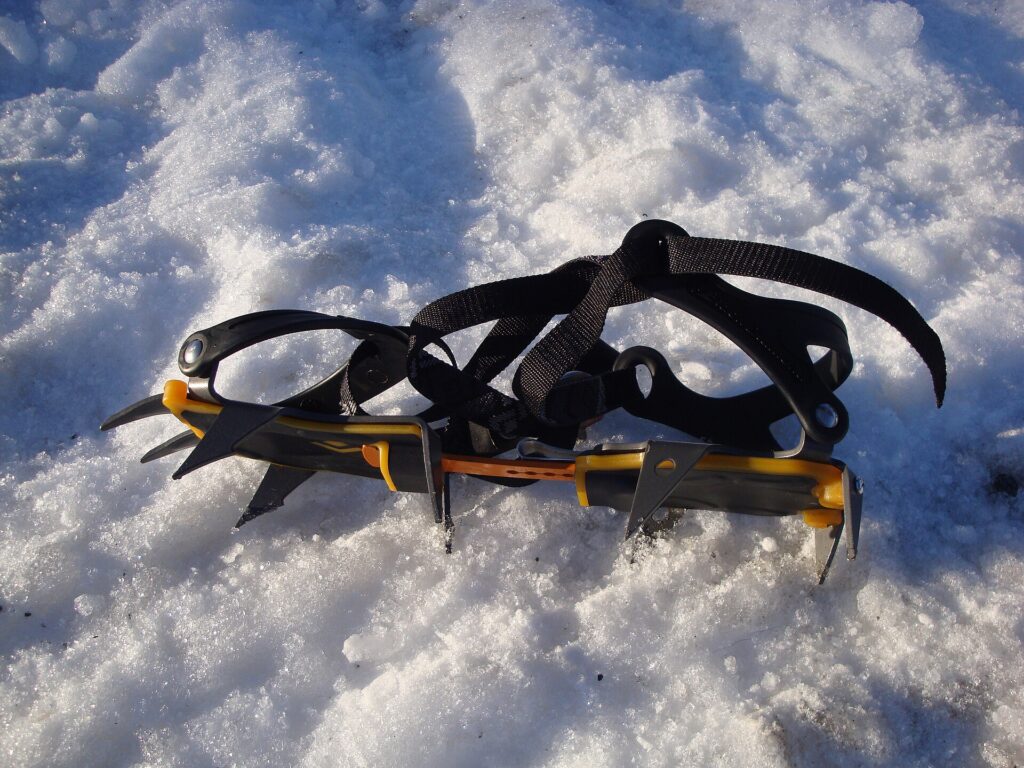 Crampones y piolet apoyados sobre nieve dura junto a una mochila de montaña