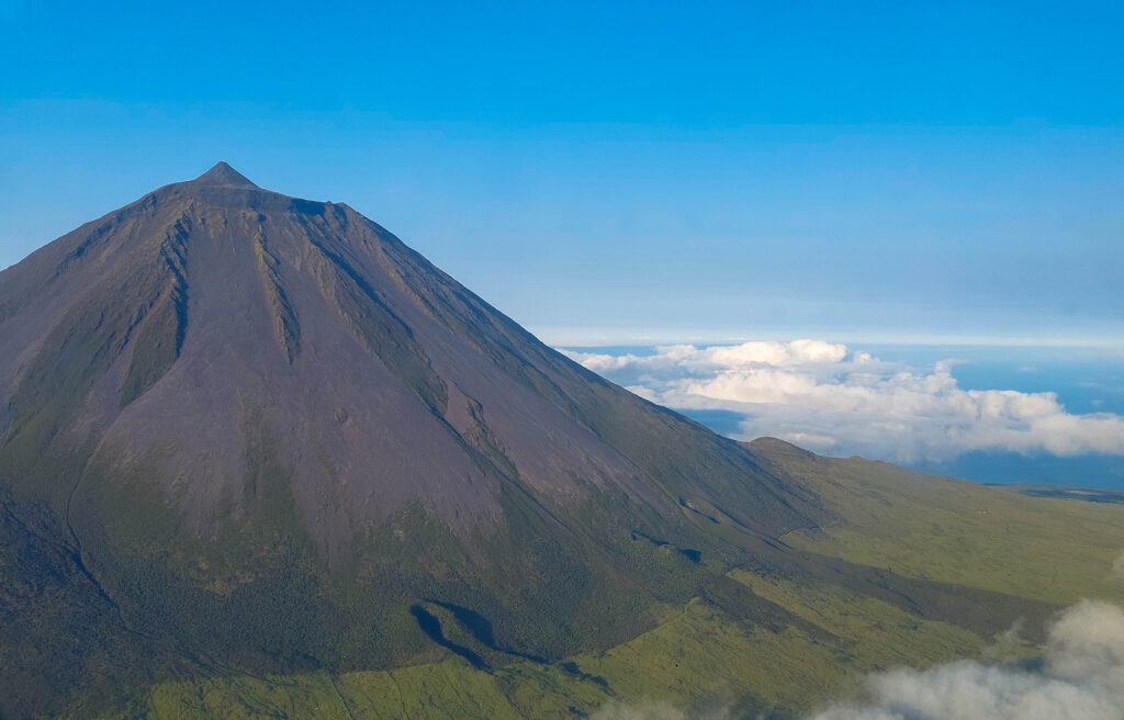 Cono volcánico oscuro con la cima parcialmente cubierta de nubes sobre un pueblo costero