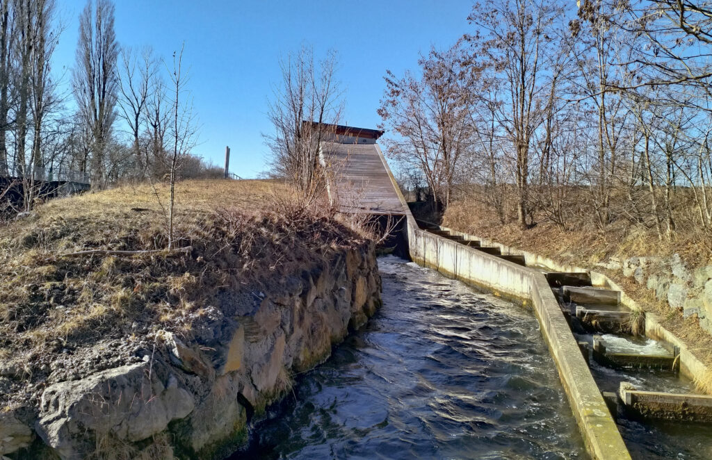 Pequeña instalación hidroeléctrica junto a un río de montaña con tubería de conducción visible